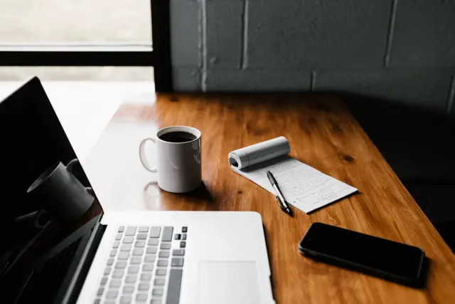 Coffee cup, notepad, and laptop on quiet minimalist desk