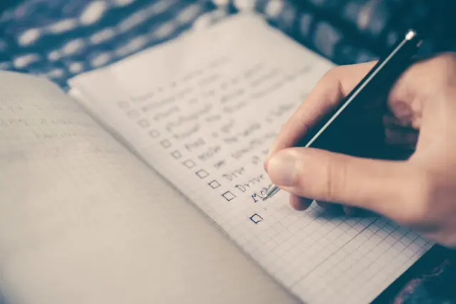 Hand writing structured daily task priorities in clean leather journal