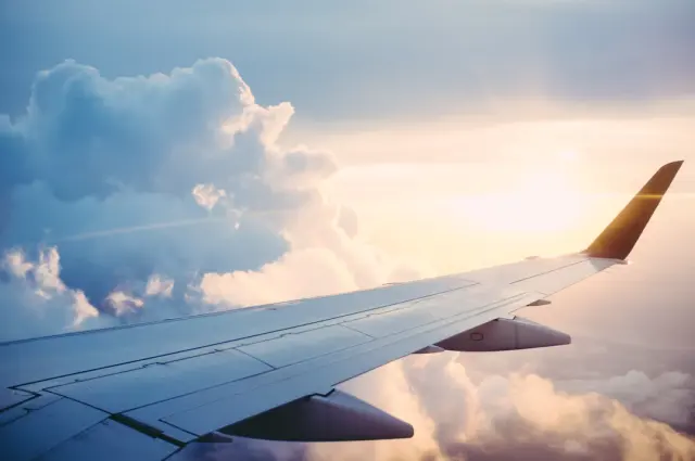 Airplane wing flying over majestic sunlit clouds during peaceful golden hour sunset