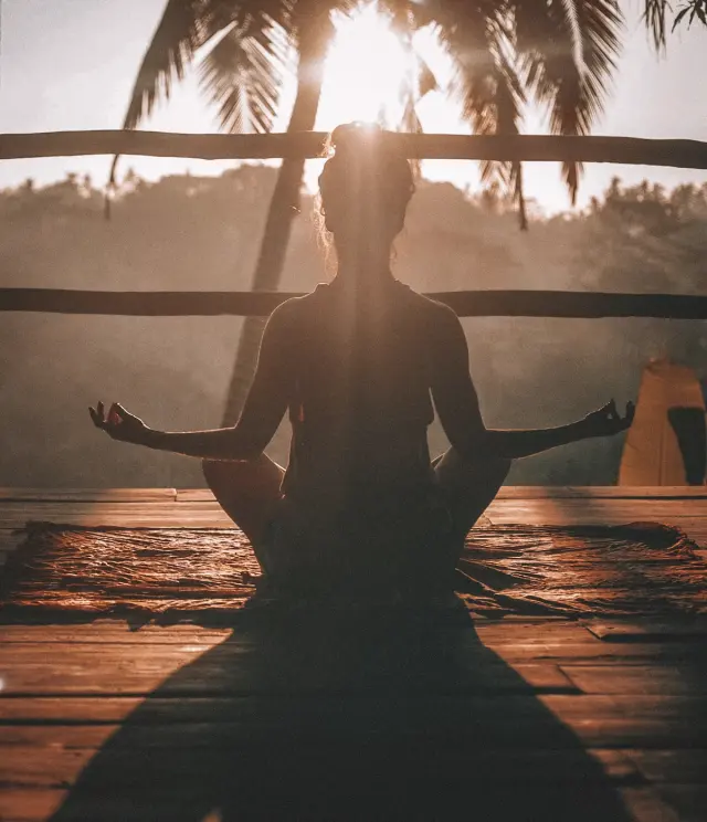 Person sitting peacefully in meditation outdoors at sunrise