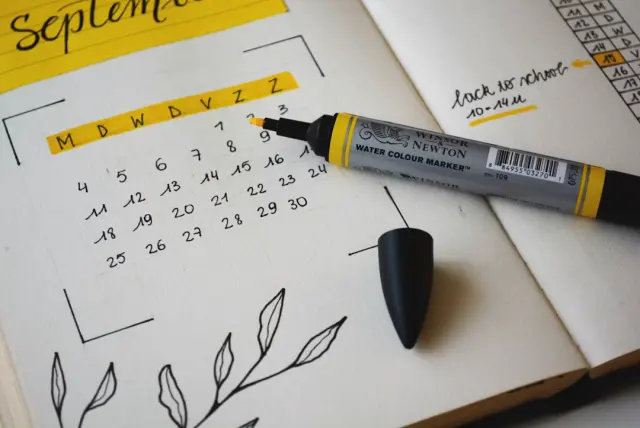 Digital calendar on laptop screen beside paper daily planner and hot espresso on desk