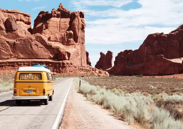 Vintage camper van parked beside scenic desert mountain highway at sunrise